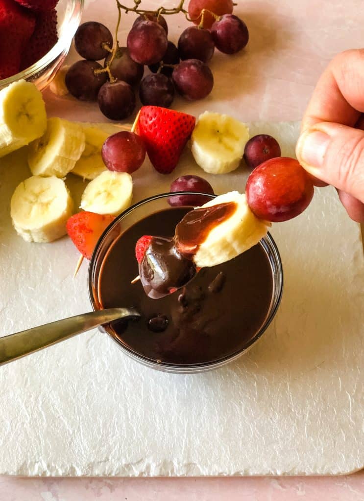dipping fruit kabob with strawberry, banana, and grape into the chocolate sauce