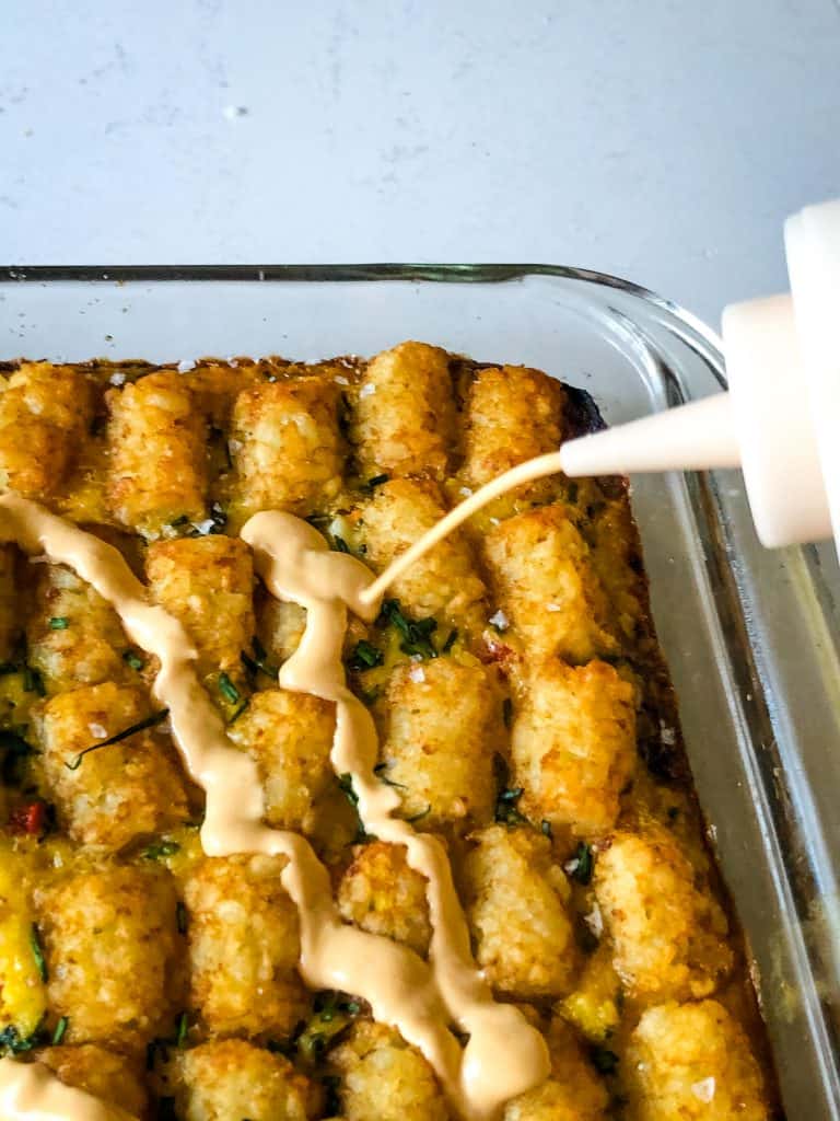 sriracha sauce being squeezed on tater tot casserole