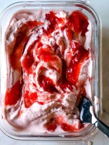 strawberry ice cream in freezer container with strawberry topping swirled in