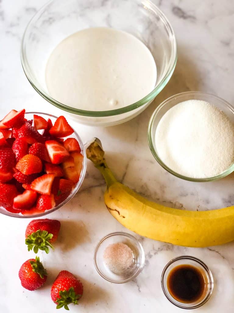 ingredients for strawberry banana ice cream including cut strawberries, banana, coconut milk, sugar, vanilla, salt