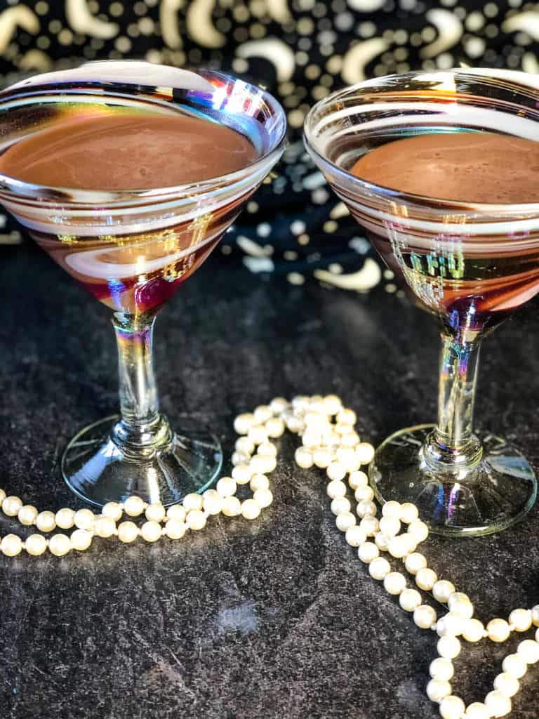 Two elegant martini glasses filled with chocolate martinis made with vegan chocolate liqueur with stars and moon backdrop and white beads in forefront
