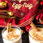 Two glasses of vegan egg-nog with cinnamon sticks against a red plaid background with christmas ornaments. with pinterest text overlay