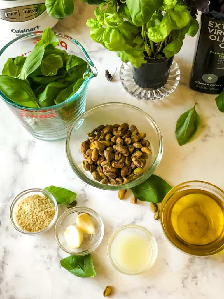 ingredients needed for vegan pistachio pesto including basil leaves, pistachios, olive oil, nutritional yeasts, garlic cloves, lemon juice