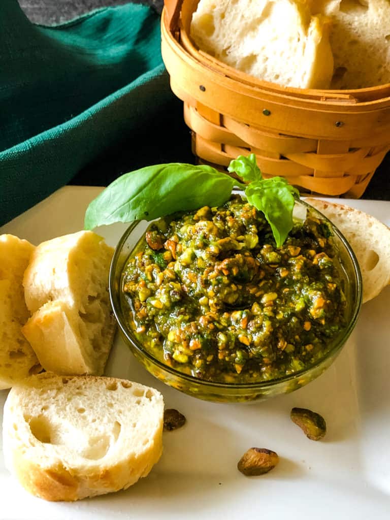 Bowl of pistachio pesto with sliced bread on which to spread this delicious pesto