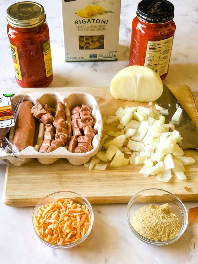 Ingredients for pasta bake including pasta,pasta sauce, chopped onion, vegan sausage, vegan cheese shreds, and nutritional yeast ,
