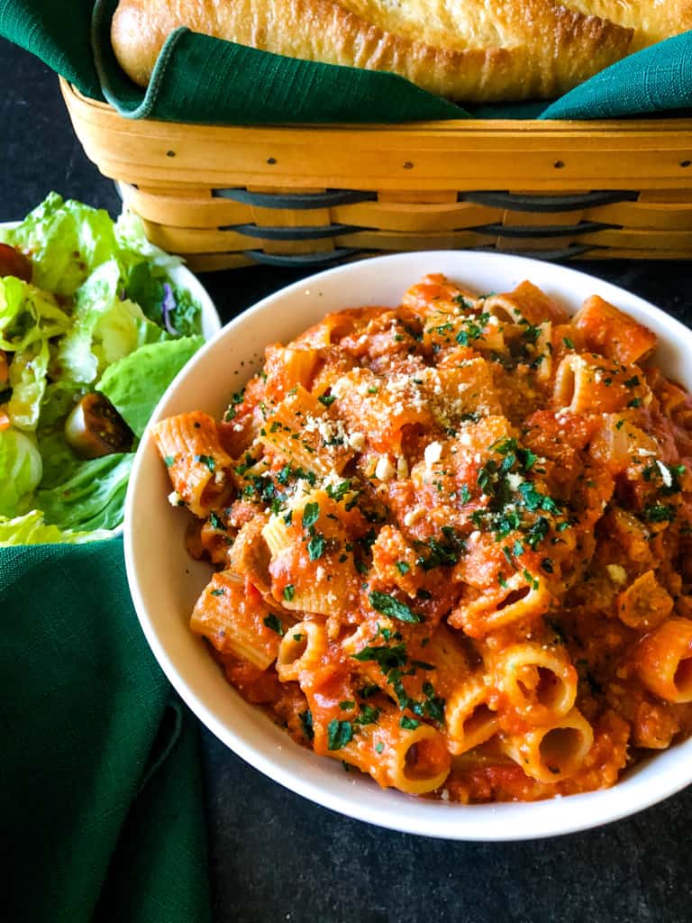 Vegan pasta bake in a dish with salad and bread in the background