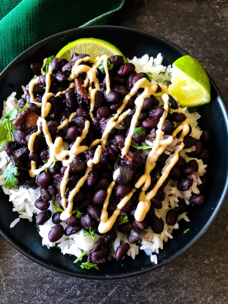 Cuban black beans over rice with limes on the side and cilantro on top drizzled with sauce