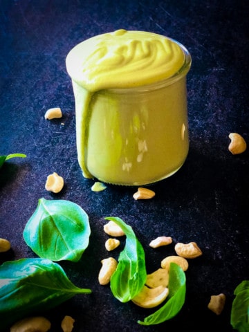 creamy basil dressing in a jar with cashews and basil leaves in the foreground