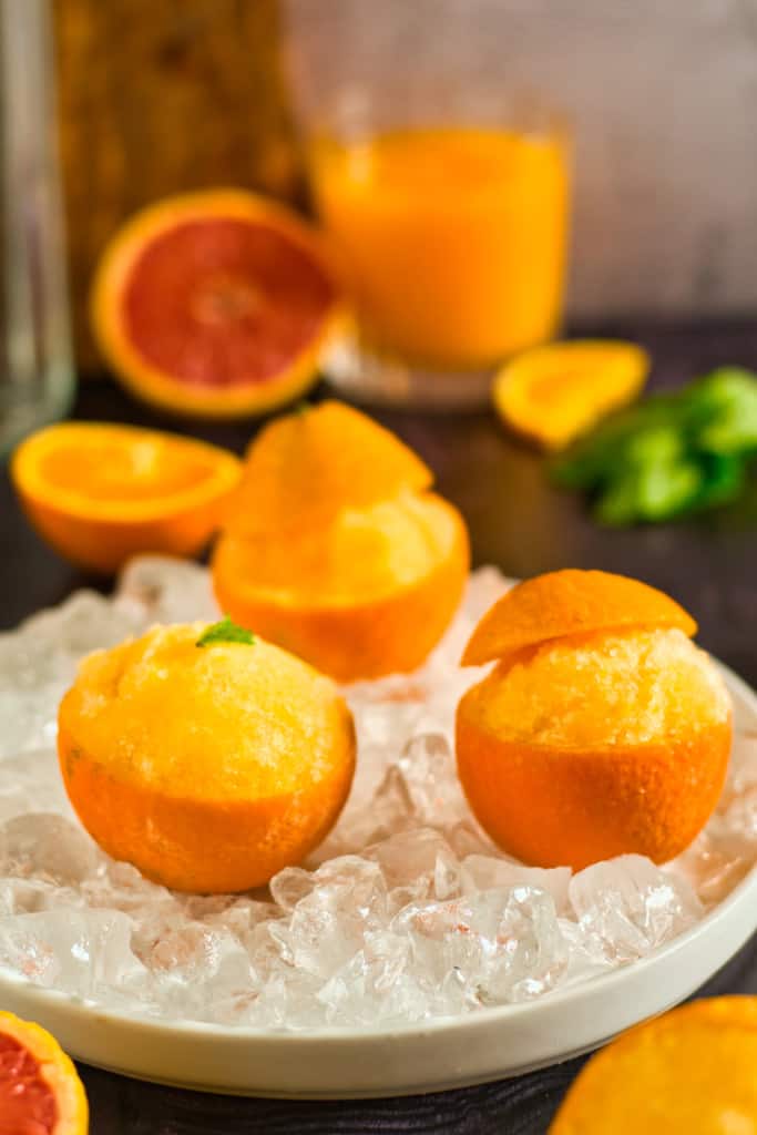 orange sorbet in orange peels in an iced dish with a glass container of orange juice in the background
