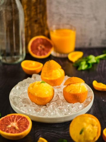 orange sorbet in orange peels in an iced dish with a glass container in the background