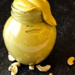 vegan honey mustard dressing in a small jar with an unsightly amount dribbling from the top with raw cashews in the foreground