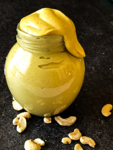 vegan honey mustard dressing in a small jar with an unsightly amount dribbling from the top with raw cashews in the foreground