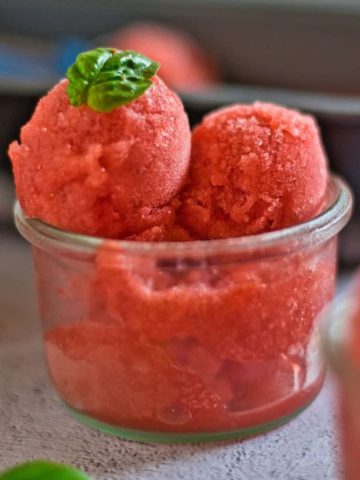 Scoops of strawberry basil sorbet in a glass ice cream dish