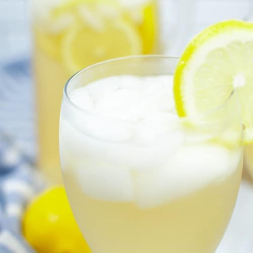 Two glasses of lemonade with a filled glass pitcher
