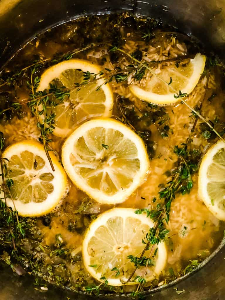 lemon herbed brown rice in the instant pot waiting to be cooked with sprigs of fresh thyme and sliced lemons on top