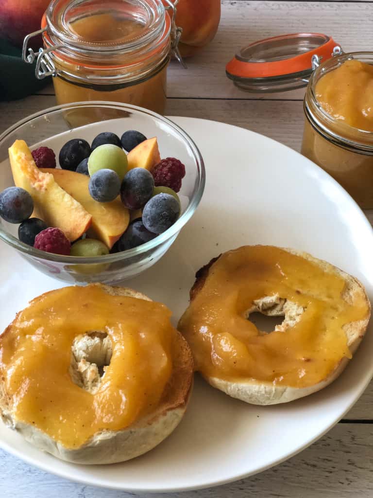 peach butter spread on bagels with a fruit dish ion the plate and two small jars of peach butter in the background