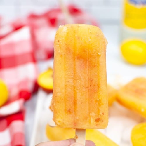 frozen peach popsicle held in hand with red checked napkin in background