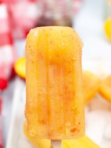 frozen peach popsicle held in hand with red checked napkin in background