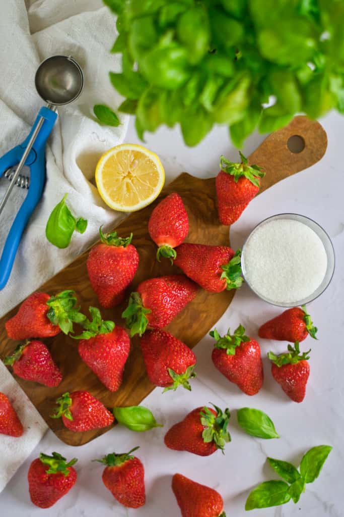 strawberries on a cutting board with basil, lemon, and sugar in the background