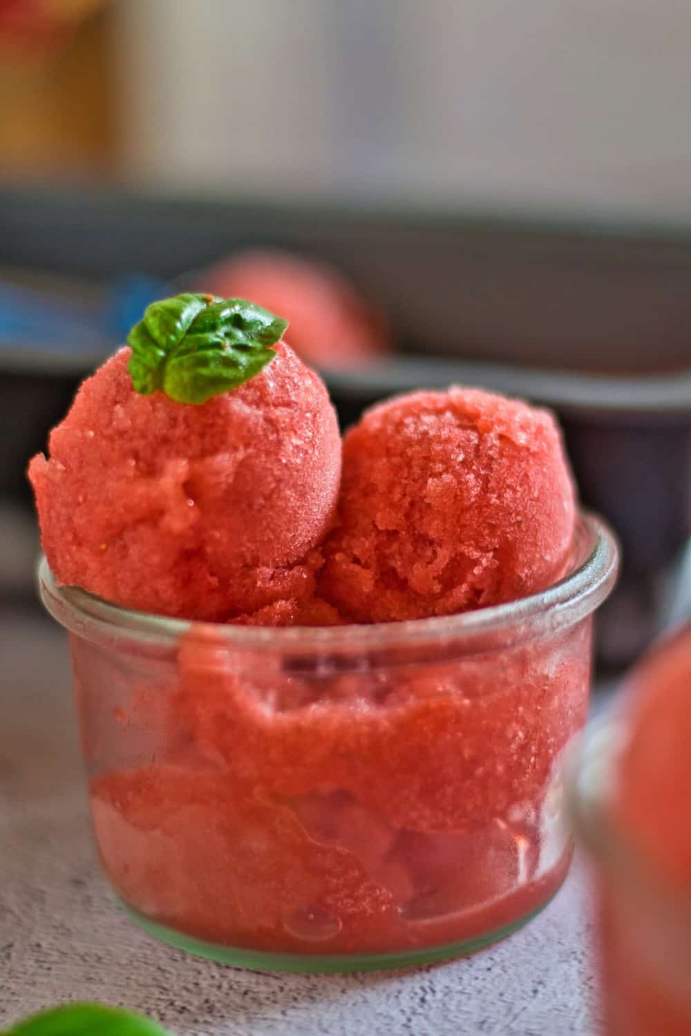 Scoops of strawberry basil sorbet in a glass ice cream dish