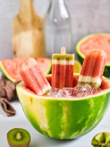 three watermelon kiwi popsicles in ice in a hollowed watermelon half