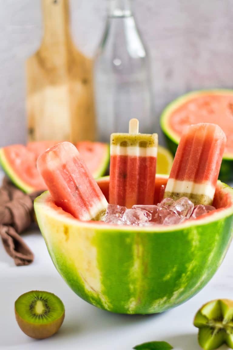 three watermelon kiwi popsicles in ice in a hollowed watermelon half