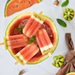 four watermelon kiwi popsicles in ice in a hollowed watermelon half