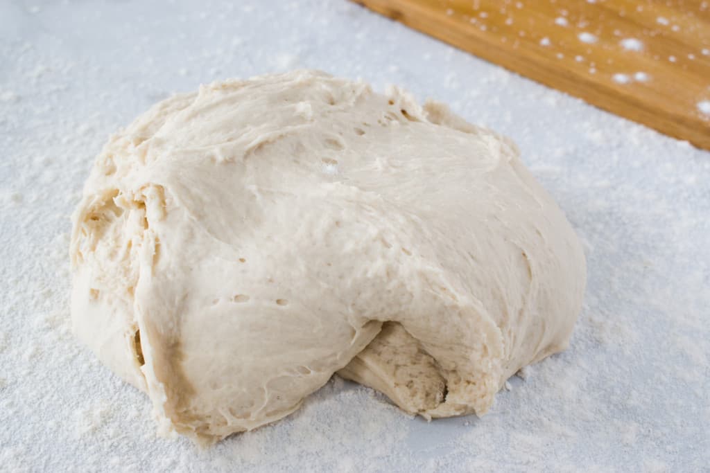 ball of uprisen pizza dough and floured wooden cutting board