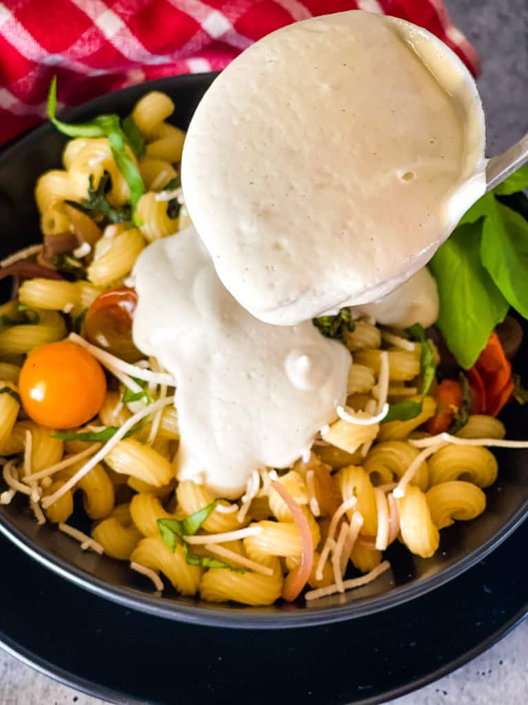 vegan alfredo sauce being poured over pasta