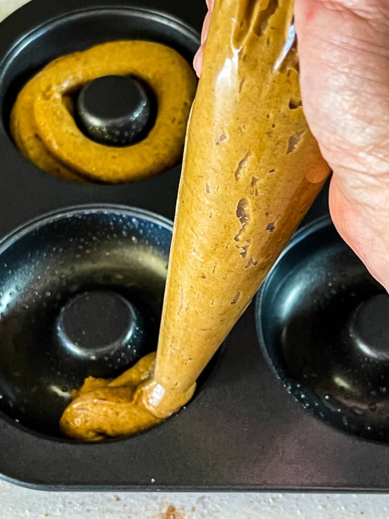 using a pastry bag to pipe in pumpkin donut batter