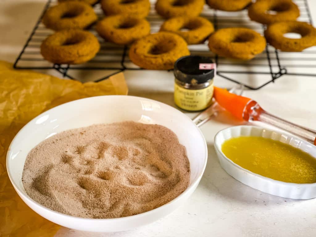 spiced sugar, melted butter with a rack of pumpkin donuts in the background