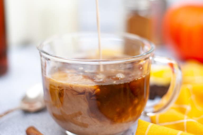 pumpkin spice creamer being poured in glass cup of coffee