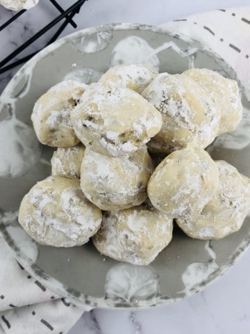 plate of snowball cookies with more on wire rack in the background