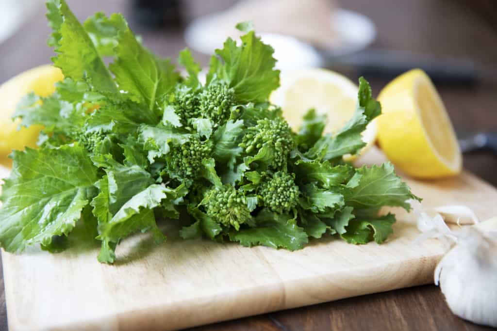 broccoli rabe on wooden cutting board with garlic and lemon in background