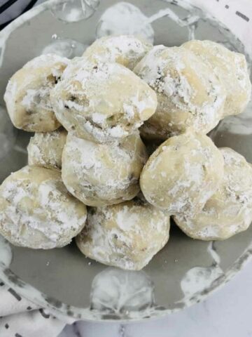 plate of snowball cookies with more on wire rack in the background