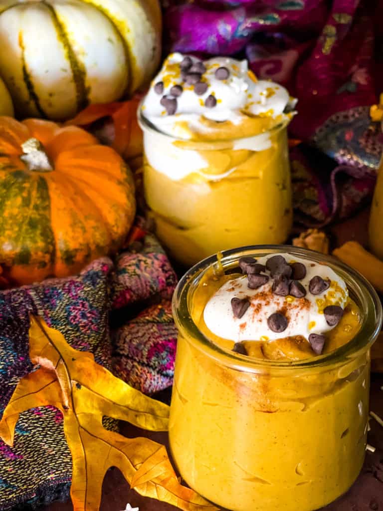 three jars of pumpkin mousse with pumpkins and fall leaves in background and cinnamon sticks in foreground