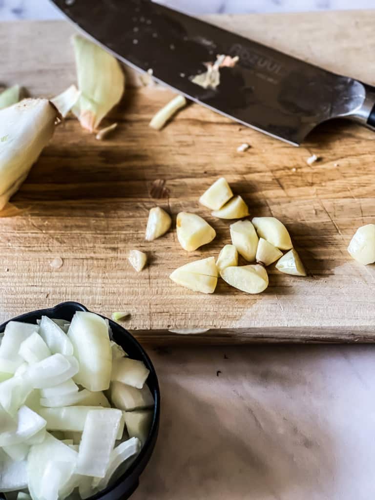chopped onions and garlic on wooden cutting board showing garlic chopped in half