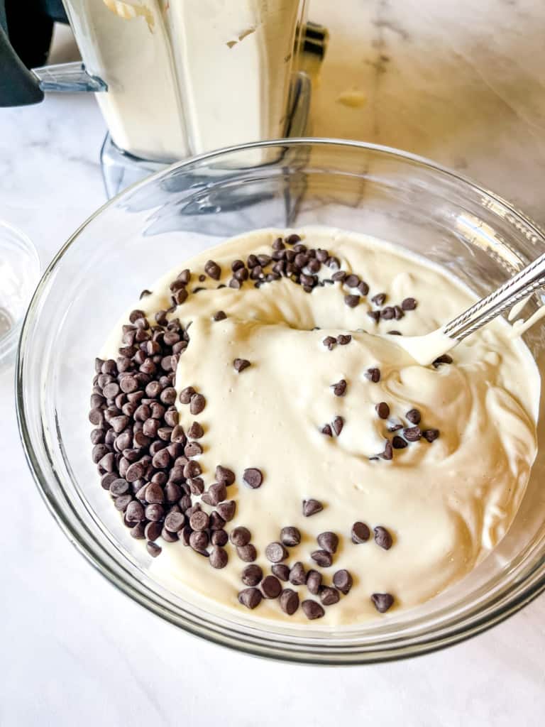 bowl of prepared cannoli cheesecake with with chocolate chips being stirred in. In the background is a blender from which the dip came.
