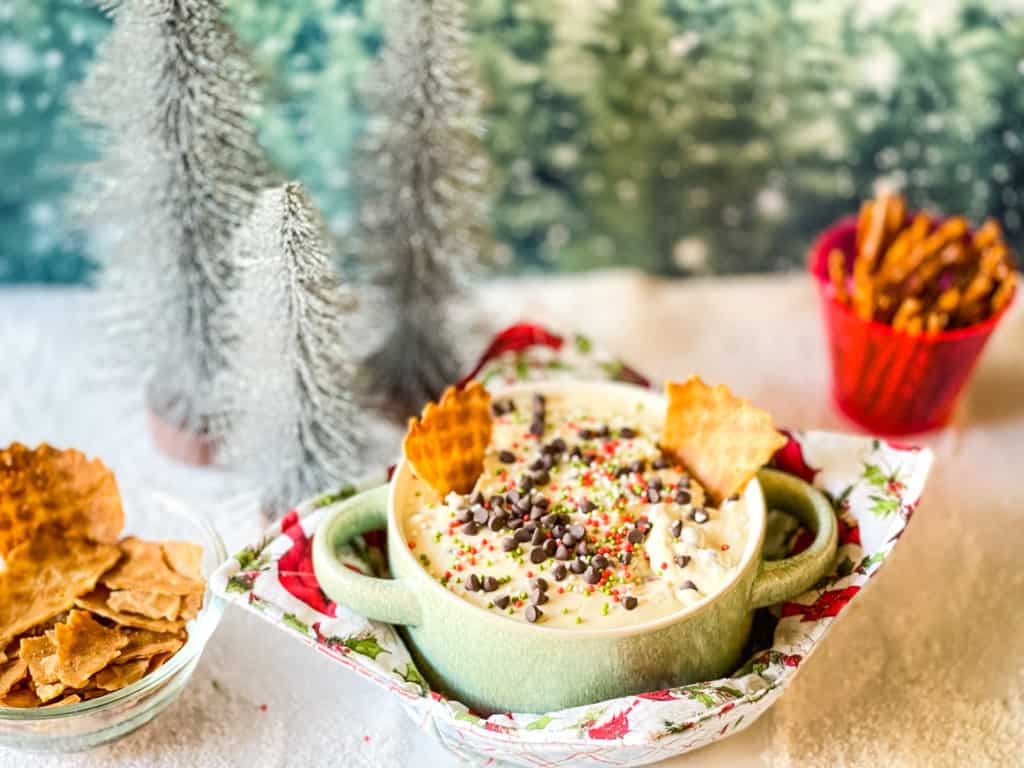 Cannoli cheesecake dip in a green bowl with festive background, pretzels, and broken sugar cones.