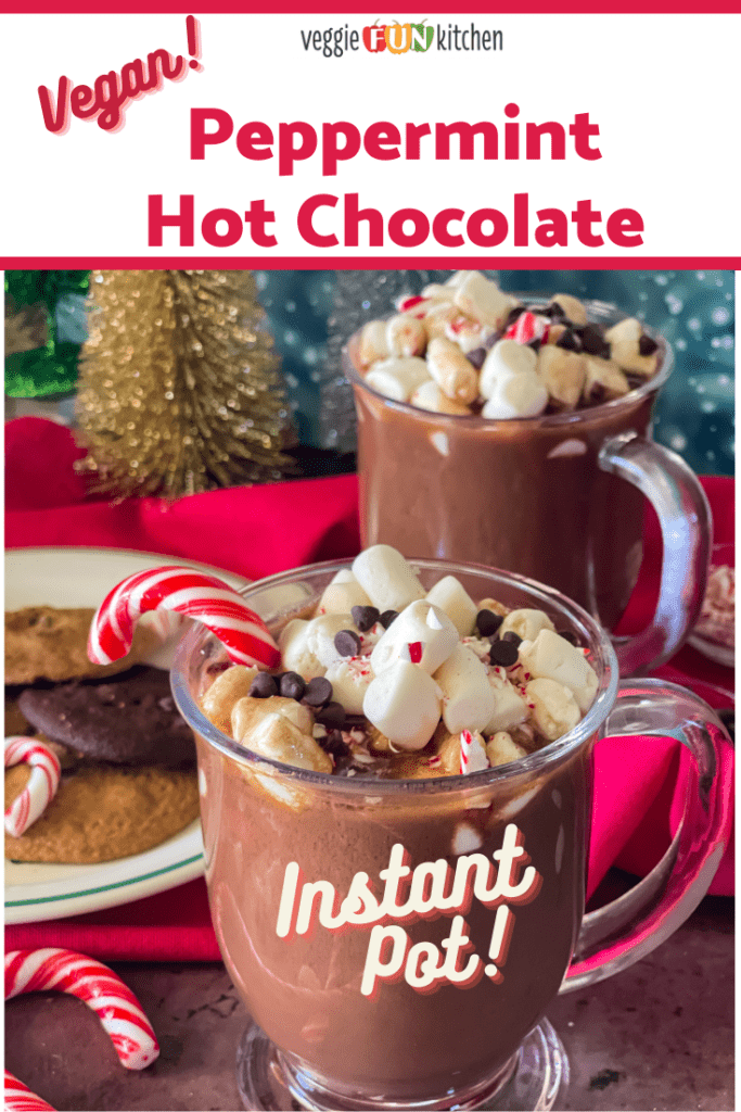 Two glass mugs of peppermint hot chocolate topped with marshmallows, mini chocolate chips, and candy canes. A plate of cookies are in the background along with festive sparkly trees all with pinterest text overlay