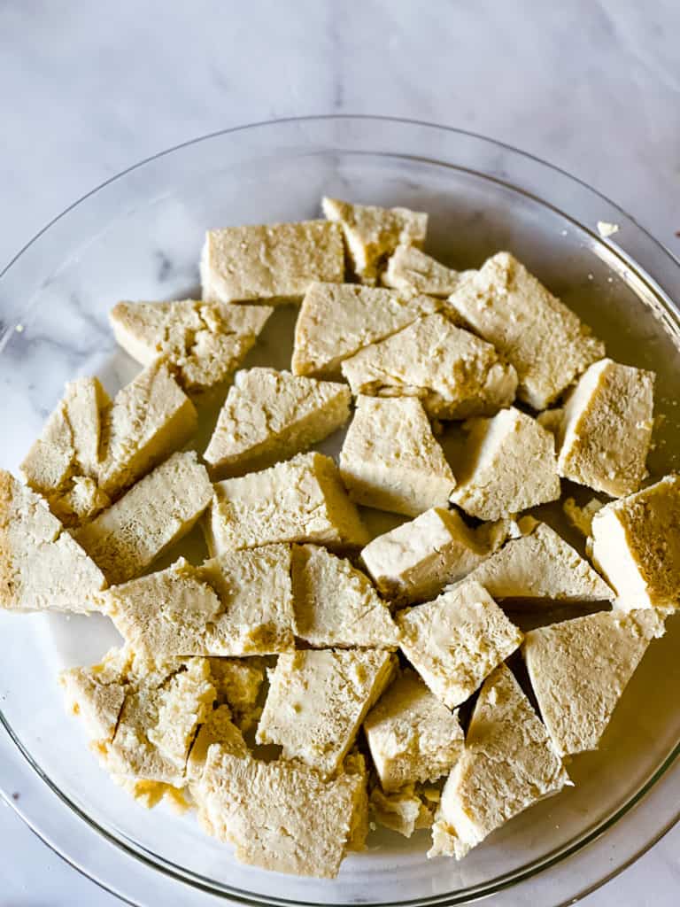 chunks of tofu in a glass pie plate waiting to be soaked