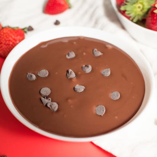 chocolate dip in white bowl with chocolate chips sprinkled on the top and a bowl of strawberries with some chocolate chips and strawberries surrounds the bowls