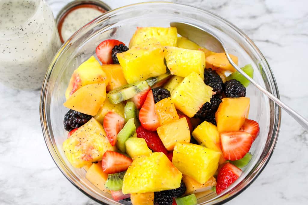 bowl of fresh fruit salad with jar of poppy seed dressing in background