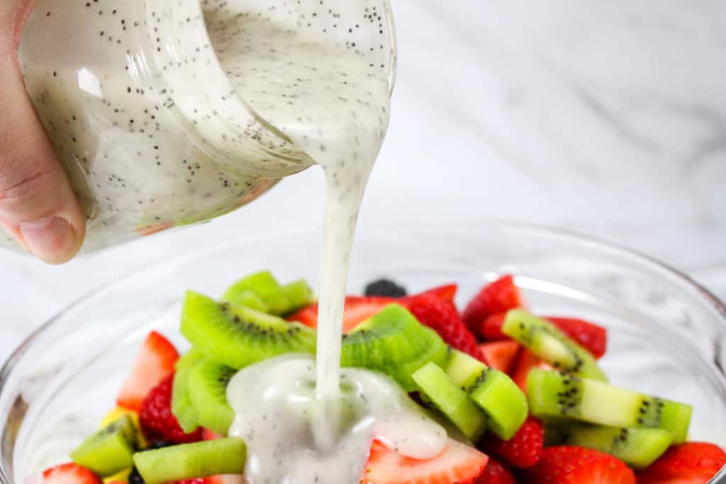pouring poppy seed dressing on the fresh fruit salad