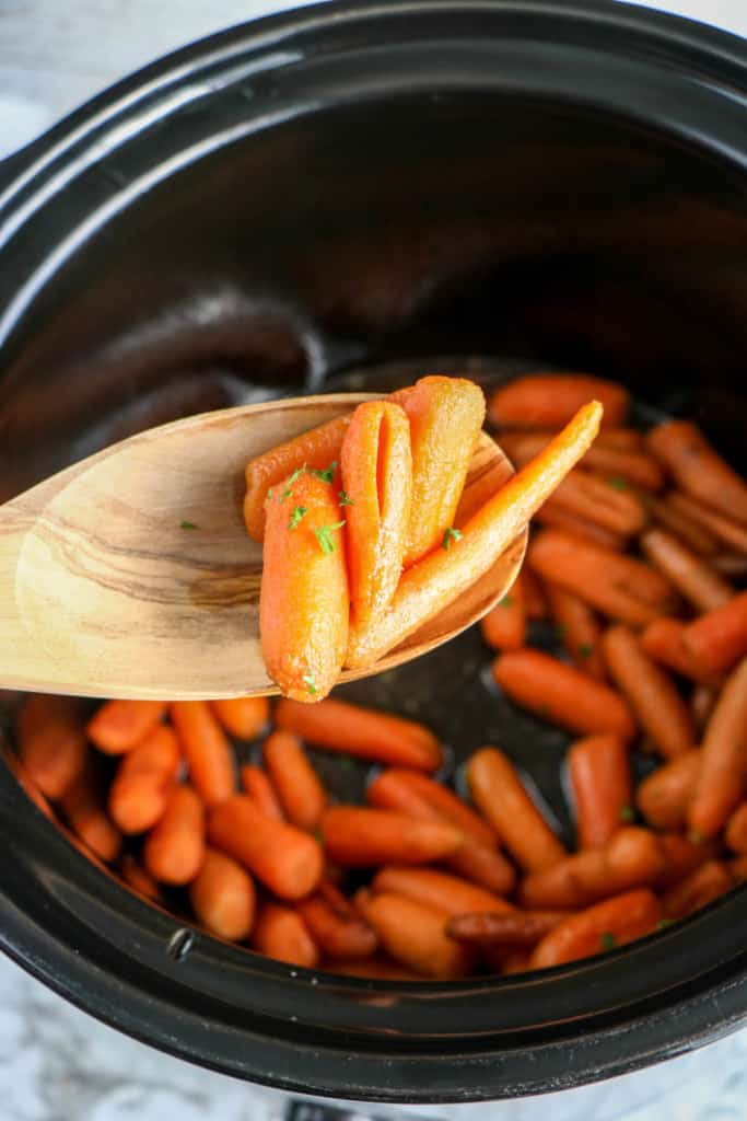 removing cooked brown sugar carrots from the slow cooker with a wooden spoon