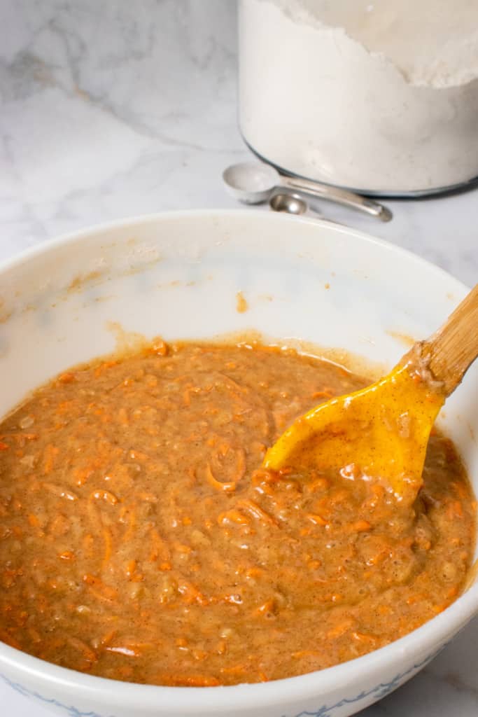 mixing the carrot cake batter in a white bowl with a wooden spoon