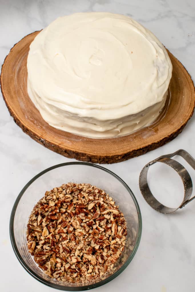 bowl of chopped pecans with chopper and frosted cake in the background