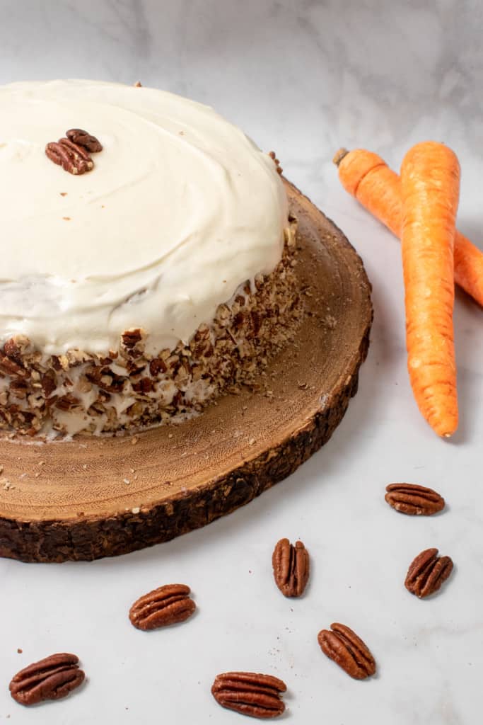 whole vegan carrot cake with pecans and carrots in background