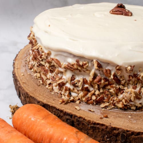 whole vegan carrot cake with pecans and carrots in background