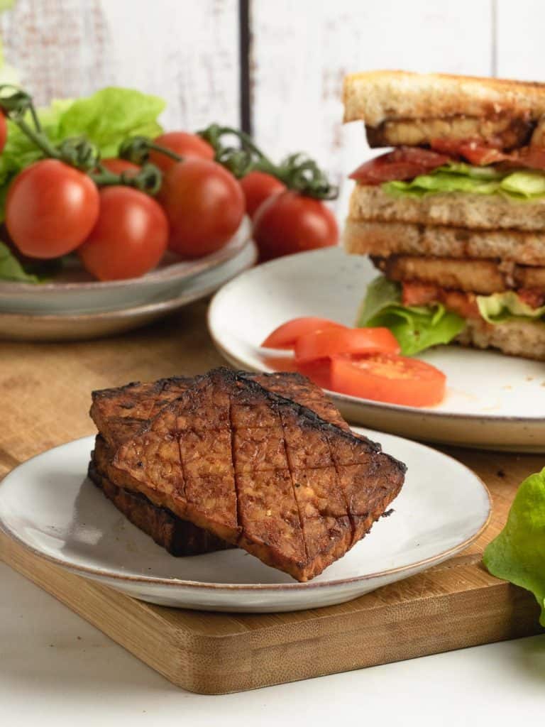 tempeh bacon in foreground with sandwich and salad in background